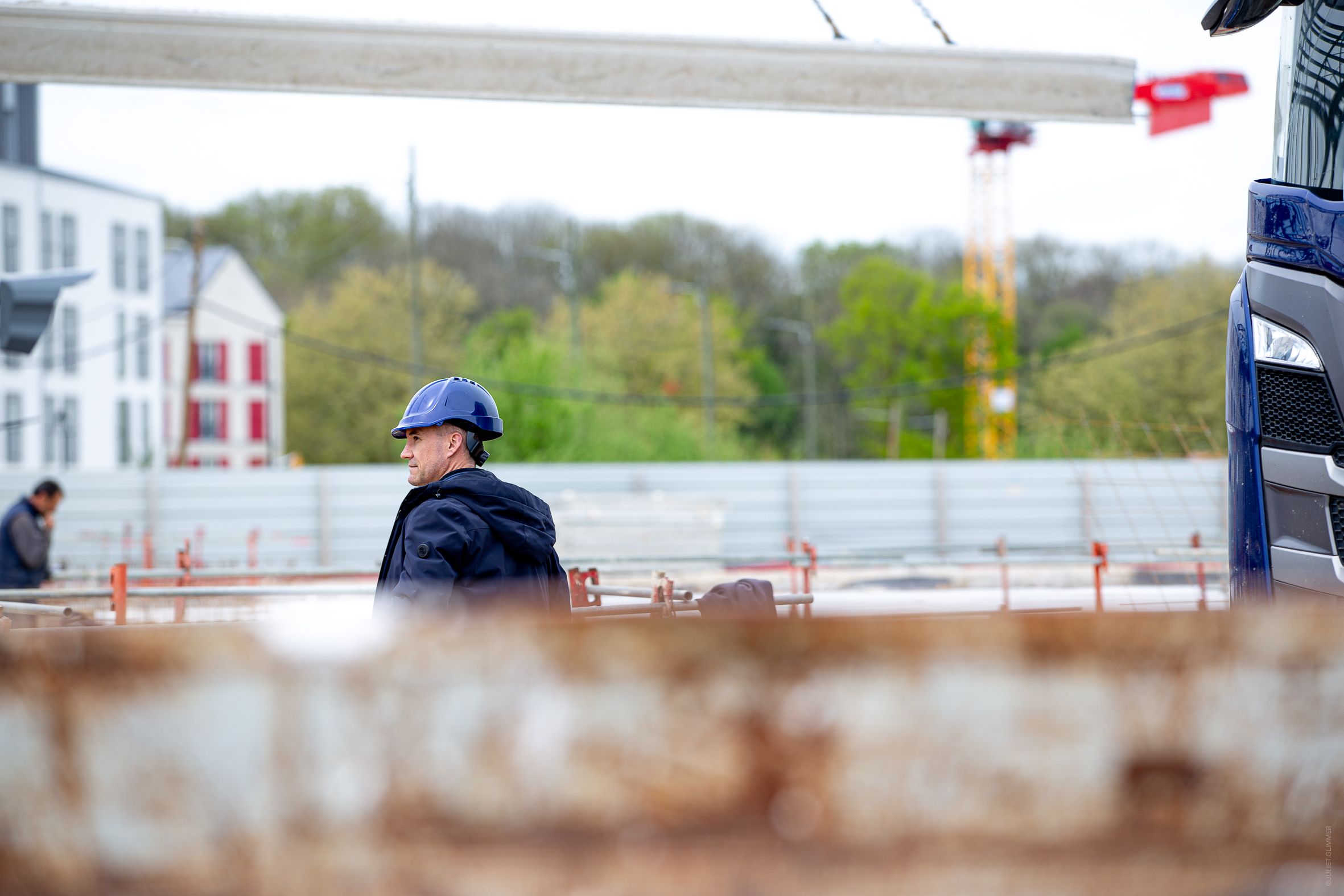 Le dirigeant d’Aedifici'hom, Nicolas DORGLER contractant général du bâtiment, en observation sur un chantier, visible au loin derrière des structures métalliques.