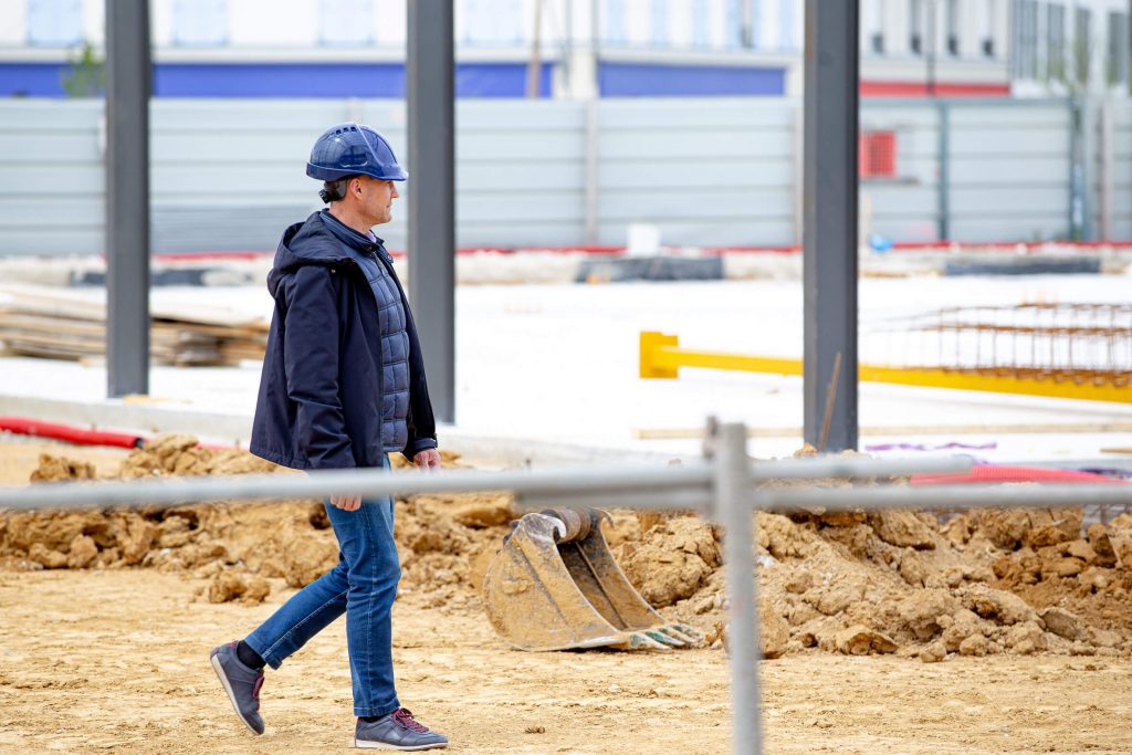 Le fondateur d’Aedifici'hom, Nicolas DORGLER contractant général du bâtiment, marche et en visite sur un chantier en phase de démarrage, les premières structures visibles.
