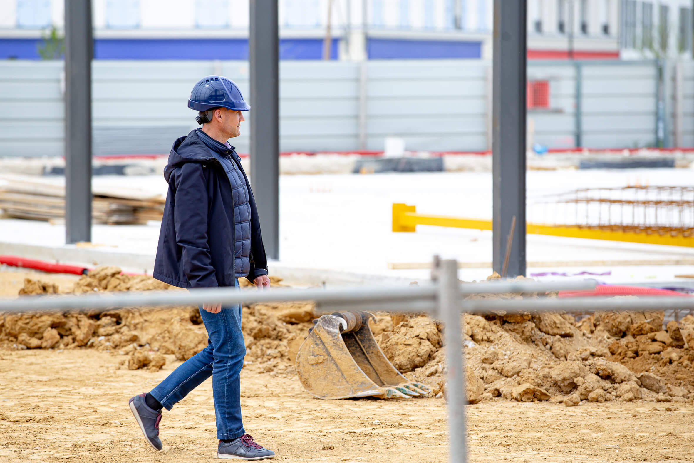 Le fondateur d’Aedifici'hom, Nicolas DORGLER contractant général du bâtiment, marche et en visite sur un chantier en phase de démarrage, les premières structures visibles.